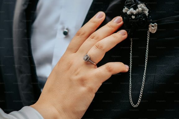 A hand gently touching a man's suit jacket, featuring decorative accessories.