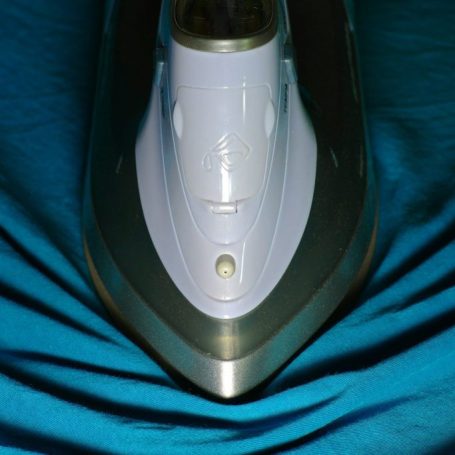 A close-up of a purple steam iron on a blue textured fabric surface.