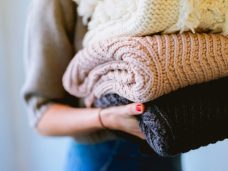 A Pressed & Fresh specialist holding a stack of folded knit blankets in soft pastel colours.
