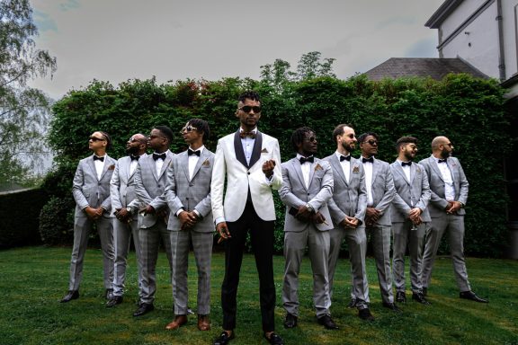 A group of men in formal suits, with one man in a white jacket standing in front.