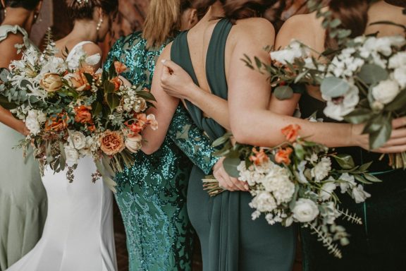 Bridesmaids in elegant dresses hold floral bouquets, celebrating a wedding together.