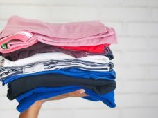 Pressed & Fresh holding a neatly stacked pile of various coloured clothes.