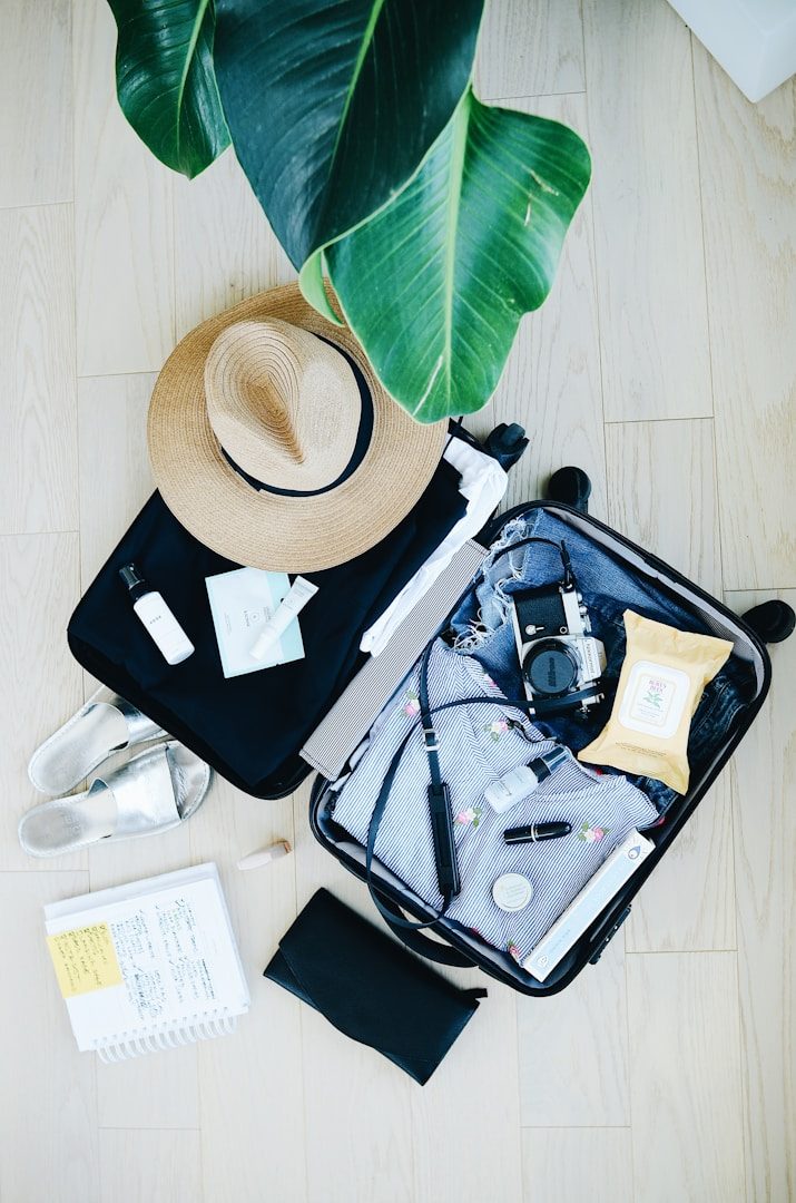 Open suitcase with a hat, laptop, cables, a notebook, and snacks on a wooden floor. Pressed & Fresh take the stress out of packing.