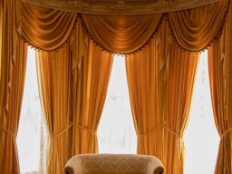 Pressed & Fresh | Ornate golden curtains frame a plush, light-coloured armchair by a window.