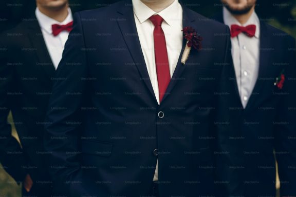 Three men in formal suits, two wearing bow ties and one with a flower lapel.