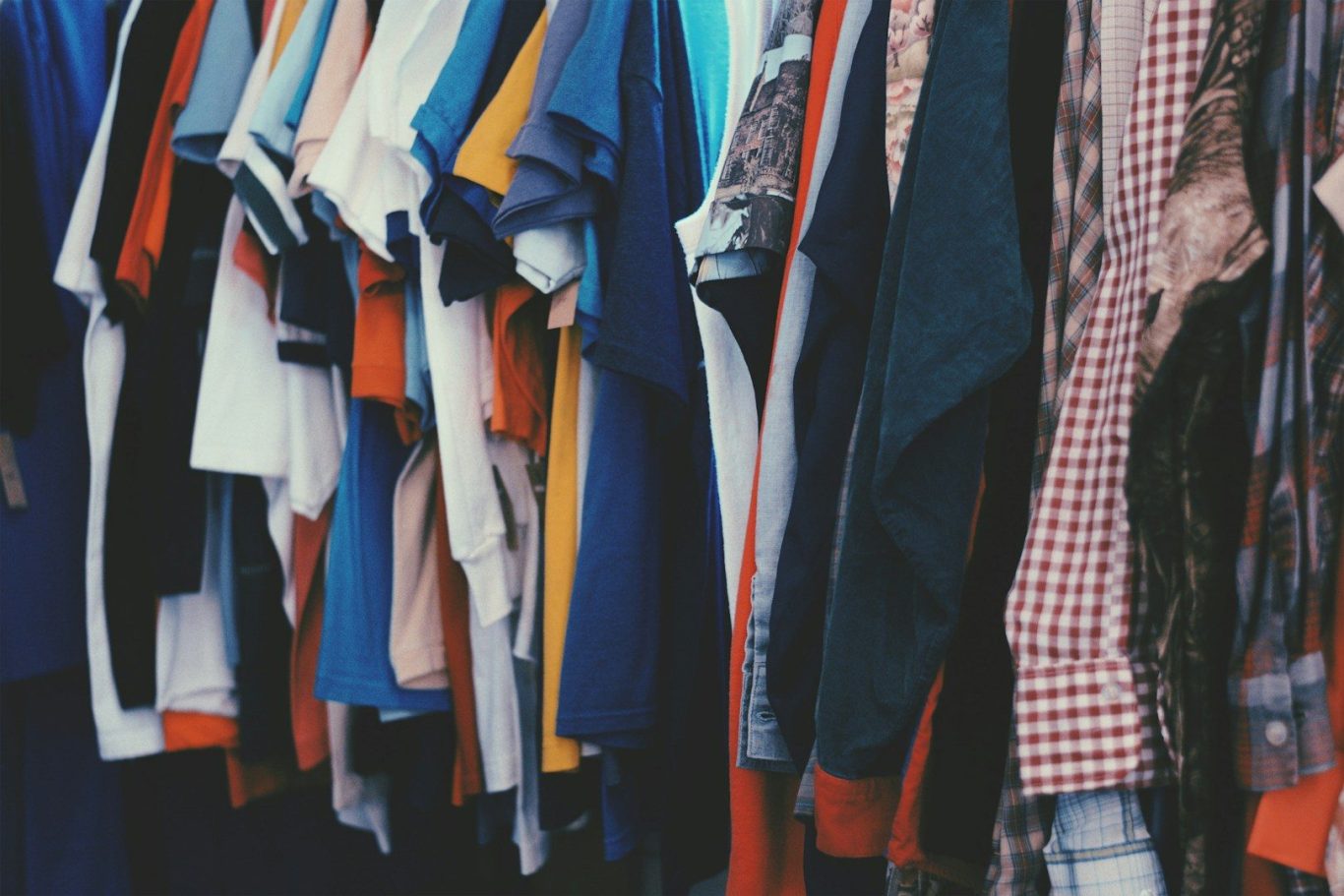 A variety of shirts in different colours and styles hanging on a rack.