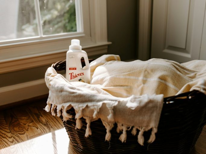 Pressed & Fresh | A wicker basket with a blanket and a bottle of laundry detergent by a window.