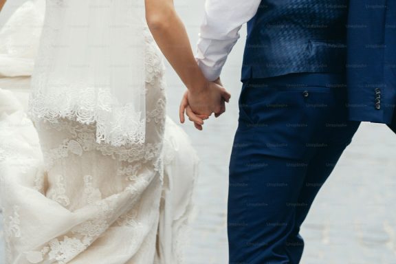 A close-up of a couple holding hands, dressed in wedding attire.