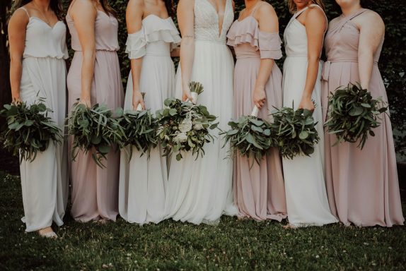 Bridesmaids in pastel dresses holding bouquets, standing together outdoors.